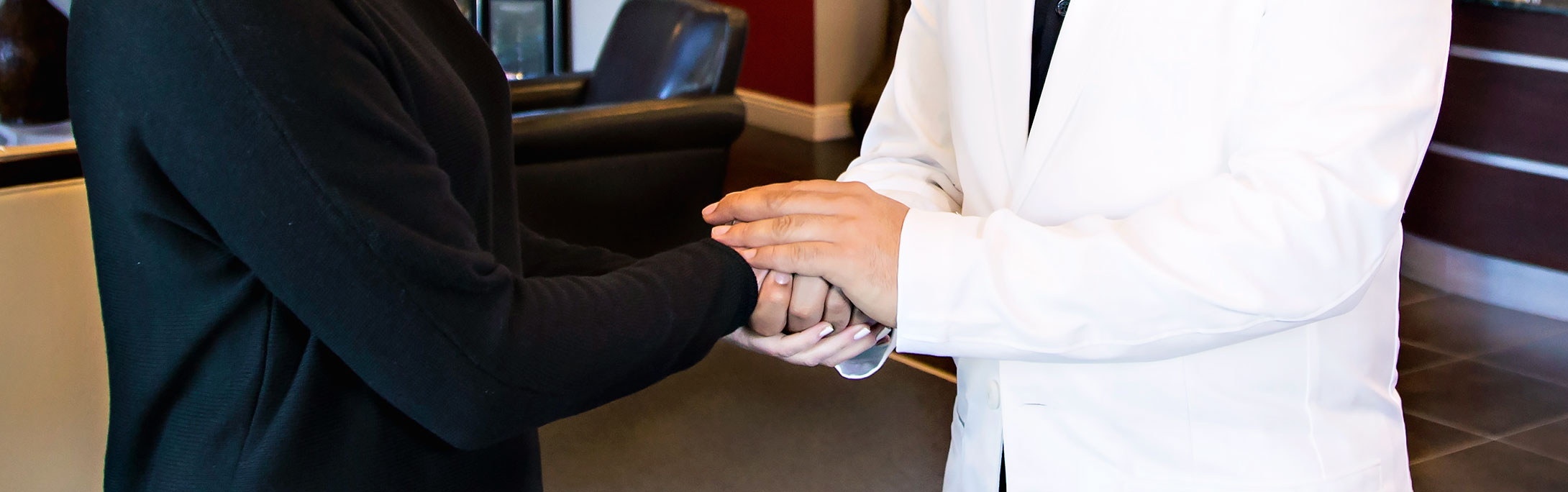 A dentist holds a woman's hand in a comforting manner.