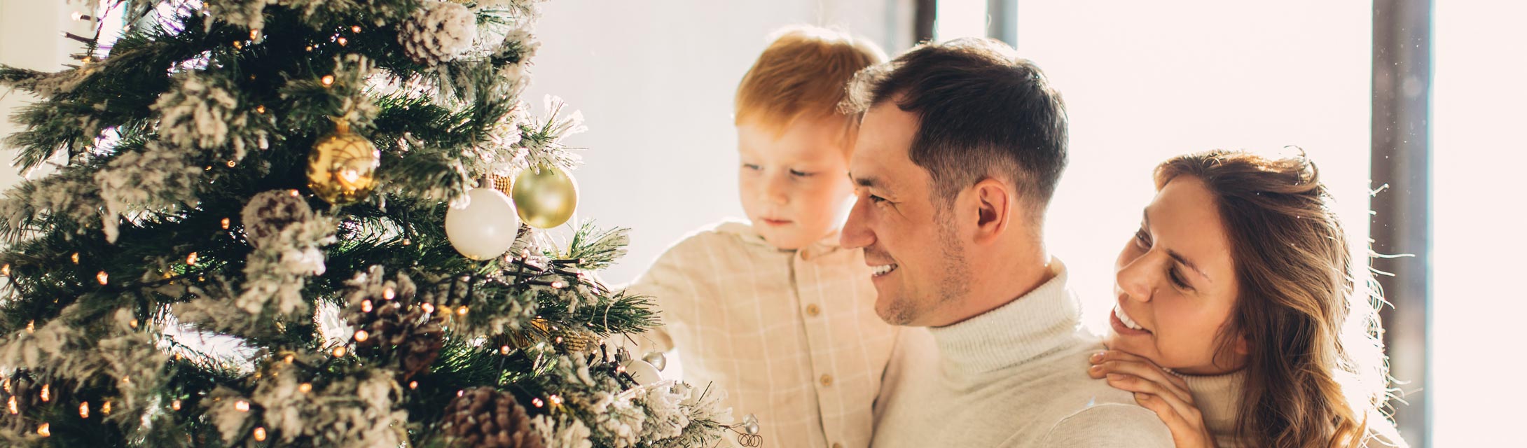 Family smiles next to their Christmas tree. Banner image for Giving the Gift of Great Smiles blog post.