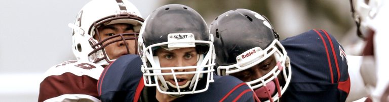 Three football players in full uniform, including athletic mouthguards, run together across a football field