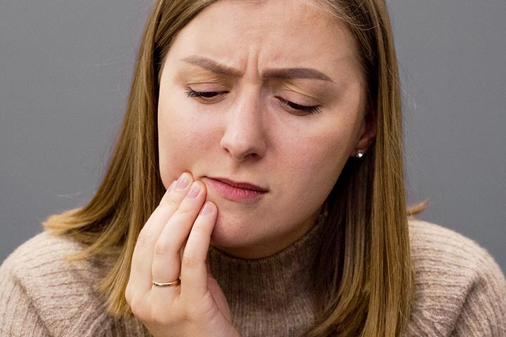 A woman holds her hand against her cheek in pain. Image for the debunking dental myths blog post