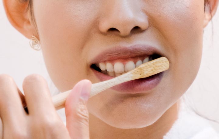 A woman brushes her teeth up close to the camera. Image for the debunking dental myths blog post