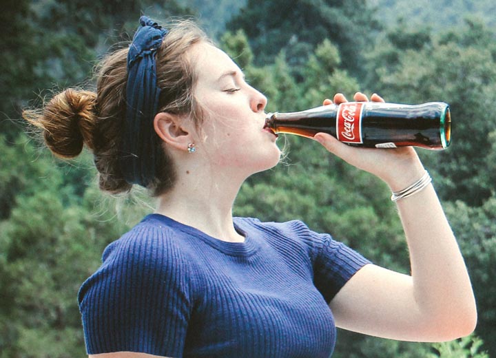 A woman drinks a bottled soda outdoors. Image for the debunking dental myths blog post